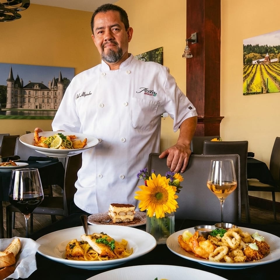 Chef presents a plated seafood dish in an elegant restaurant dining room surrounded by pasta, fried seafood, wine, and sunflowers.